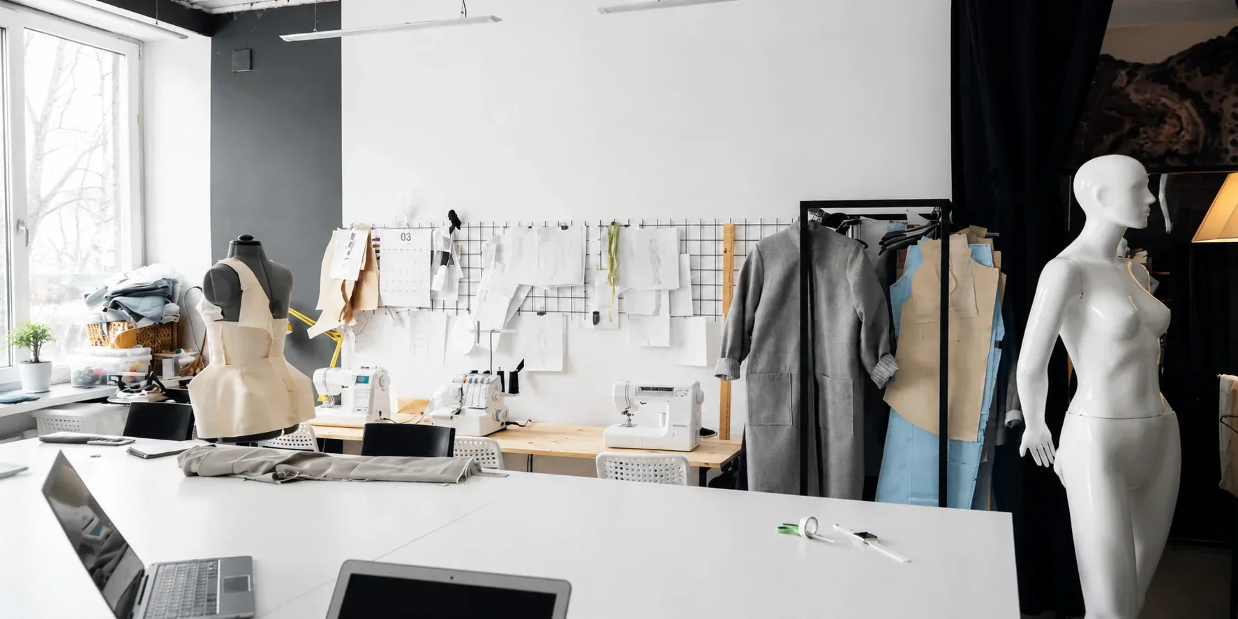 Fashion design studio with sewing machines, garment samples, patterns, and workspace setup